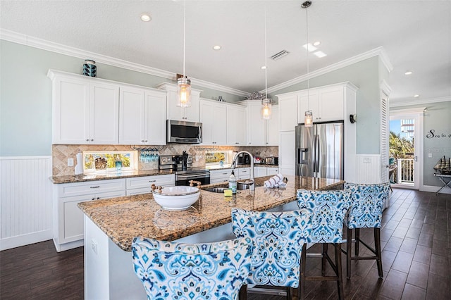 kitchen with white cabinetry, stainless steel appliances, a kitchen breakfast bar, decorative light fixtures, and a large island with sink