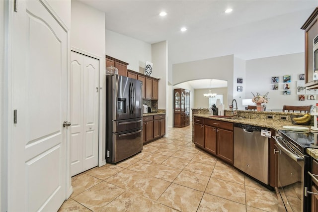 kitchen featuring appliances with stainless steel finishes, light stone counters, dark brown cabinetry, sink, and backsplash