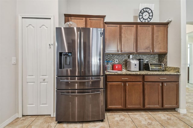 kitchen with stainless steel refrigerator with ice dispenser, decorative backsplash, light tile patterned floors, and light stone counters