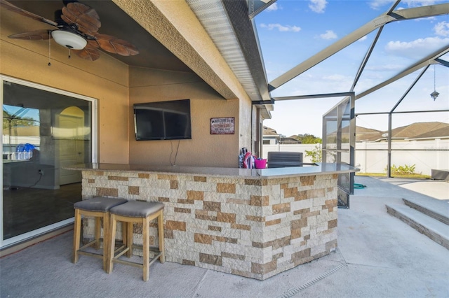 view of patio with ceiling fan, an outdoor bar, and glass enclosure