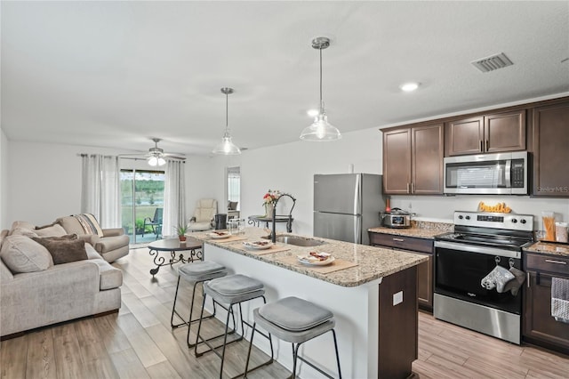 kitchen featuring stainless steel appliances, an island with sink, decorative light fixtures, and sink