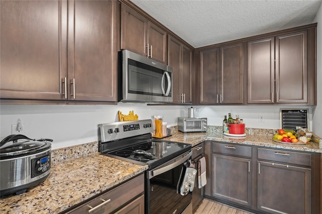 kitchen with light stone counters, dark brown cabinets, stainless steel appliances, and light hardwood / wood-style floors