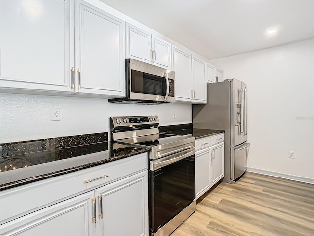 kitchen with dark stone counters, stainless steel appliances, white cabinetry, and light wood-type flooring