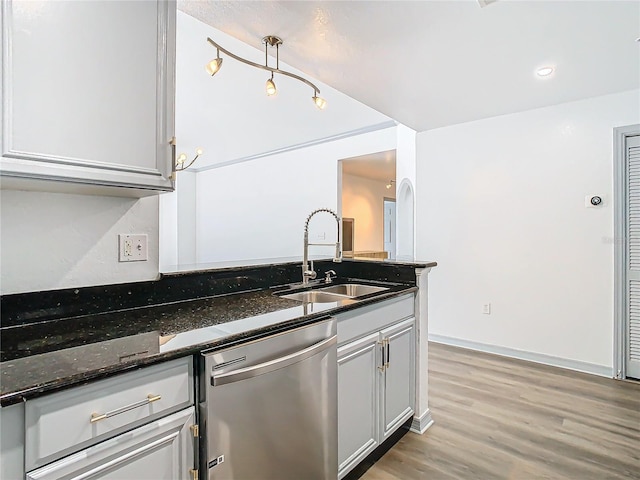 kitchen featuring dishwasher, light hardwood / wood-style floors, hanging light fixtures, dark stone counters, and sink