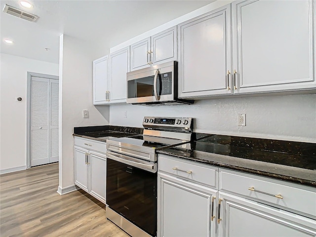 kitchen with stainless steel appliances, dark stone countertops, white cabinetry, and light wood-type flooring