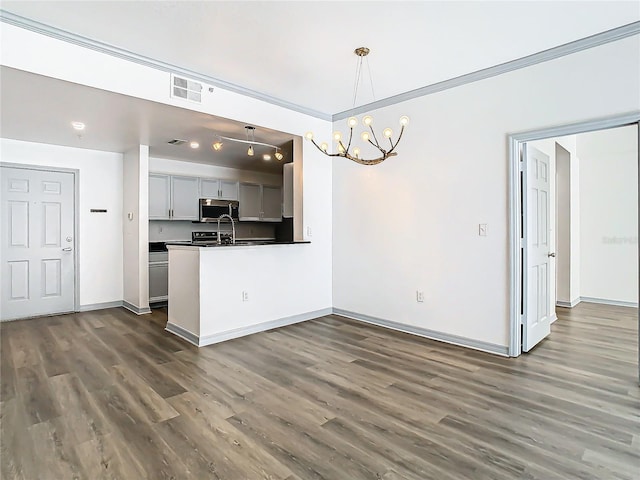 kitchen with kitchen peninsula, dark hardwood / wood-style floors, hanging light fixtures, a notable chandelier, and crown molding