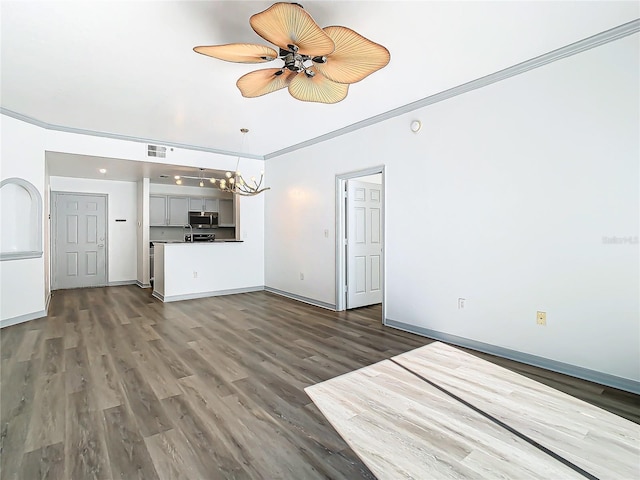 unfurnished living room with ceiling fan with notable chandelier, dark wood-type flooring, and ornamental molding