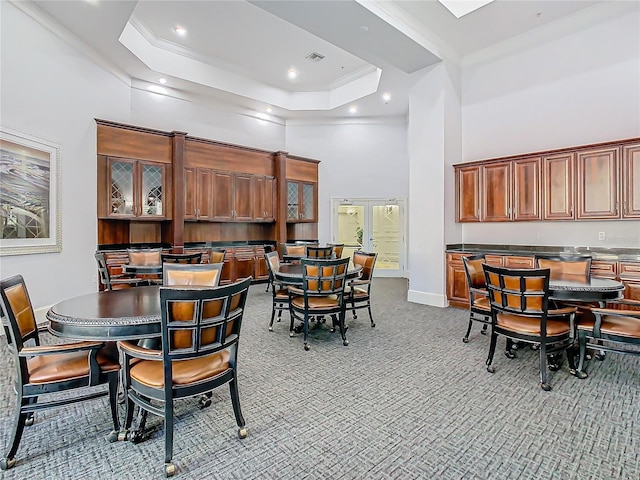 dining room with a high ceiling, a raised ceiling, light colored carpet, and ornamental molding