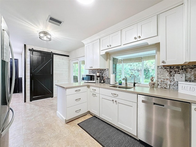 kitchen featuring sink, appliances with stainless steel finishes, white cabinets, a barn door, and kitchen peninsula