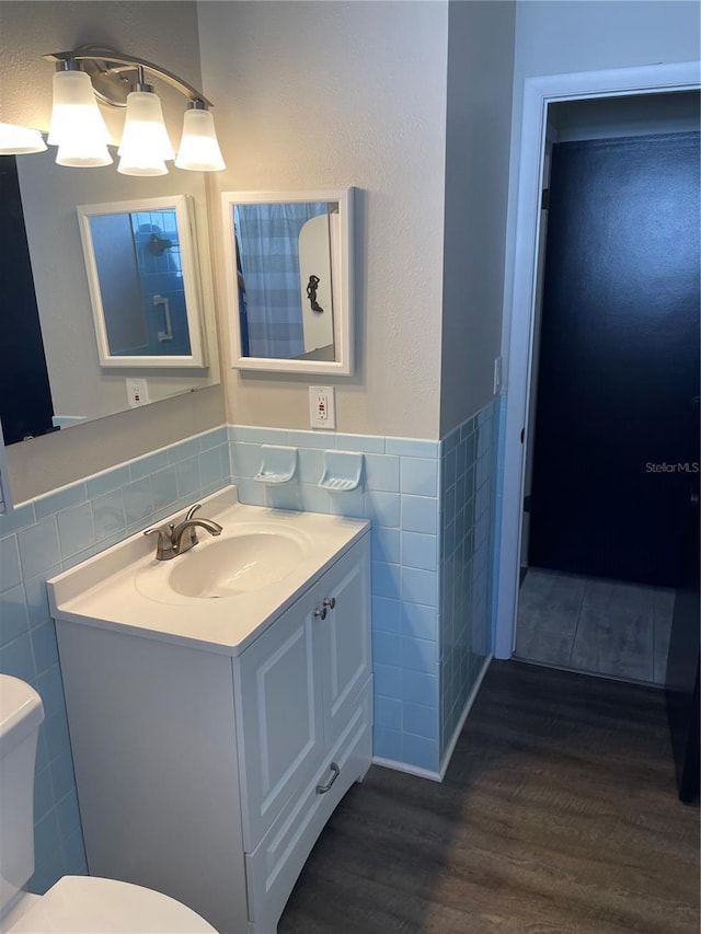 bathroom with wood-type flooring, tile walls, vanity, and toilet