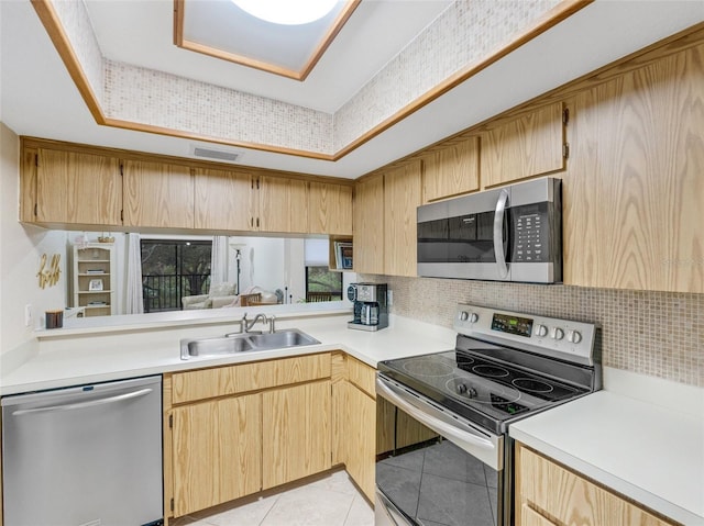 kitchen featuring appliances with stainless steel finishes, light tile patterned floors, light brown cabinetry, sink, and backsplash