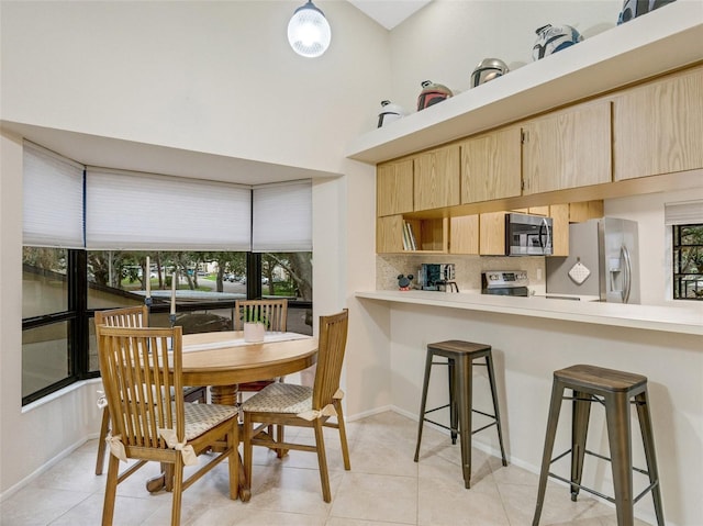 interior space with stainless steel appliances, light brown cabinetry, light tile patterned floors, backsplash, and a breakfast bar area