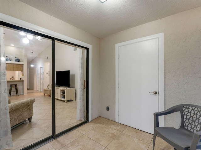 doorway featuring vaulted ceiling, light tile patterned flooring, and a textured ceiling