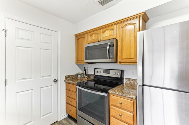 kitchen featuring dark hardwood / wood-style flooring, dark stone counters, a textured ceiling, and appliances with stainless steel finishes