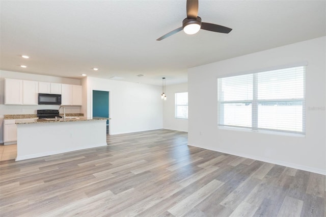 kitchen with black appliances, pendant lighting, a center island with sink, light hardwood / wood-style floors, and white cabinetry