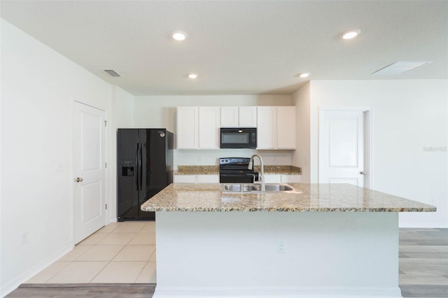 kitchen featuring light stone countertops, a kitchen island with sink, sink, black appliances, and white cabinetry