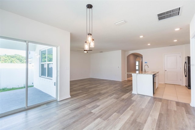 kitchen featuring a kitchen island with sink, black appliances, light hardwood / wood-style flooring, decorative light fixtures, and light stone counters