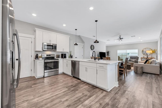 kitchen featuring kitchen peninsula, stainless steel appliances, white cabinetry, and hanging light fixtures