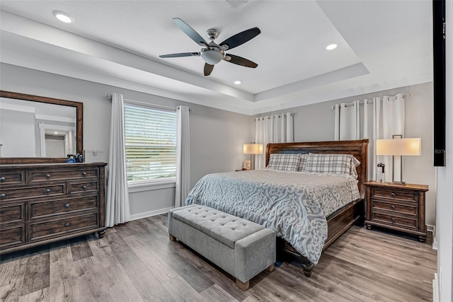 bedroom with ceiling fan, wood-type flooring, and a raised ceiling