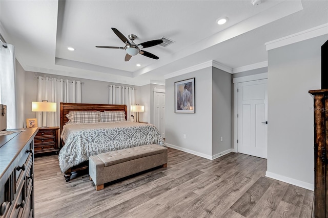 bedroom featuring ceiling fan, a tray ceiling, a closet, crown molding, and light hardwood / wood-style flooring