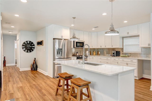 kitchen featuring stainless steel appliances, white cabinetry, decorative light fixtures, and a center island with sink