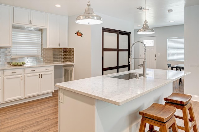 kitchen with sink, a center island with sink, white cabinetry, and pendant lighting