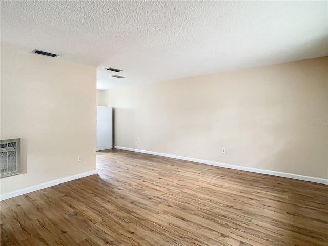 unfurnished room with hardwood / wood-style flooring, a textured ceiling, and heating unit