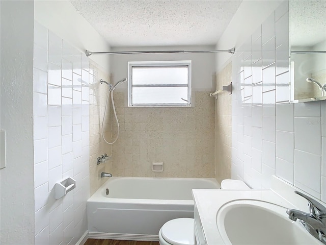 full bathroom featuring a textured ceiling, toilet, tiled shower / bath, and vanity