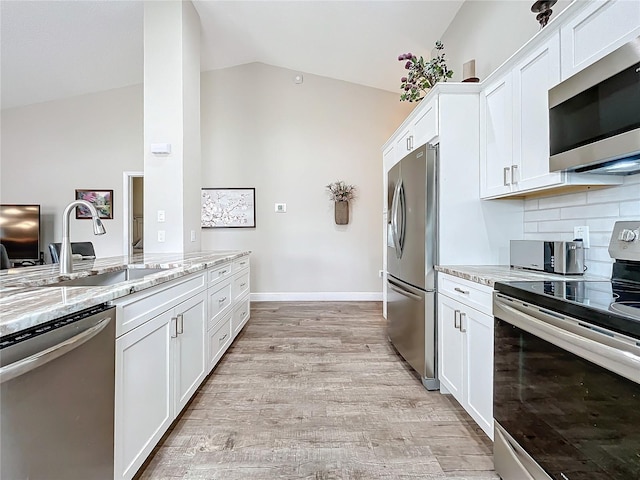 kitchen featuring vaulted ceiling, white cabinetry, appliances with stainless steel finishes, and light stone counters