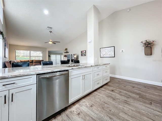 kitchen featuring white cabinets, lofted ceiling, light wood-type flooring, light stone counters, and stainless steel dishwasher