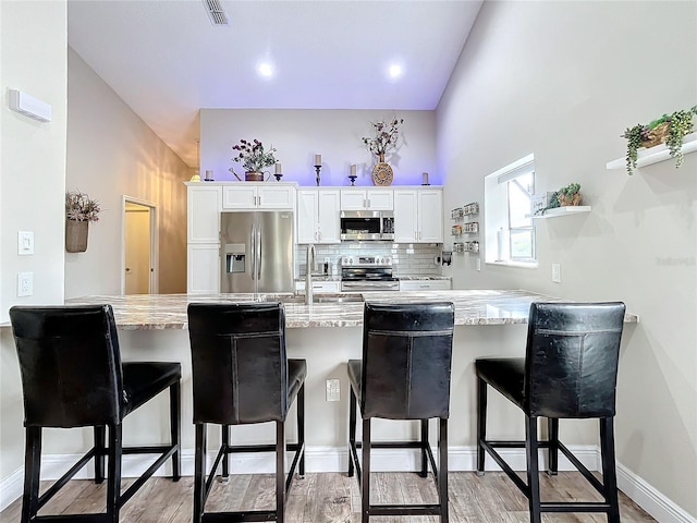 kitchen featuring kitchen peninsula, white cabinets, a breakfast bar, and stainless steel appliances