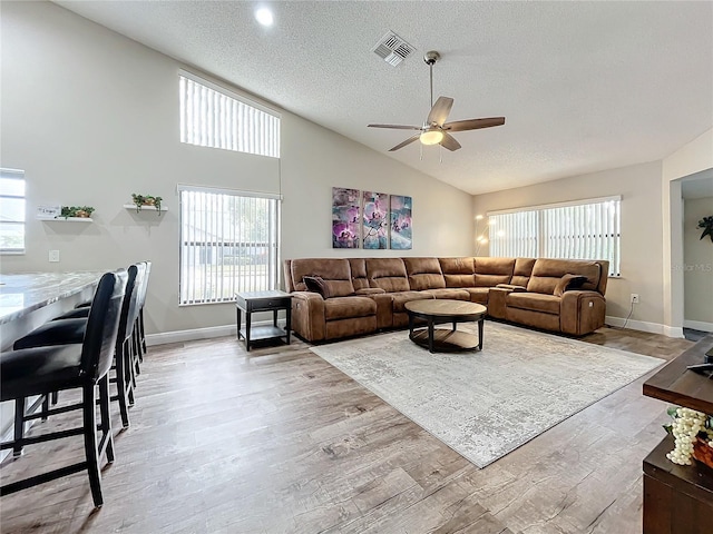 living room with a textured ceiling, ceiling fan, light wood-type flooring, and high vaulted ceiling