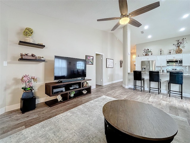 living room featuring a textured ceiling, ceiling fan, light hardwood / wood-style flooring, and high vaulted ceiling