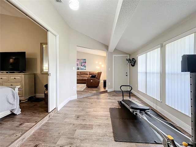 exercise room featuring vaulted ceiling, a textured ceiling, and light hardwood / wood-style floors