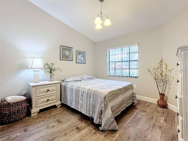 bedroom featuring hardwood / wood-style flooring, lofted ceiling, and an inviting chandelier