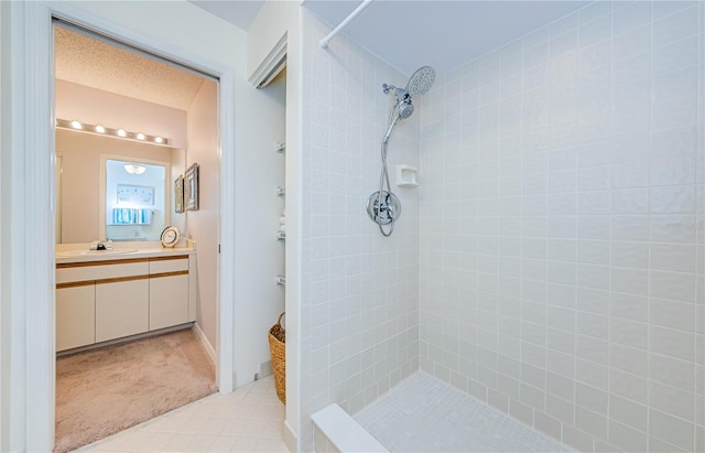 bathroom featuring a textured ceiling, tiled shower, and vanity