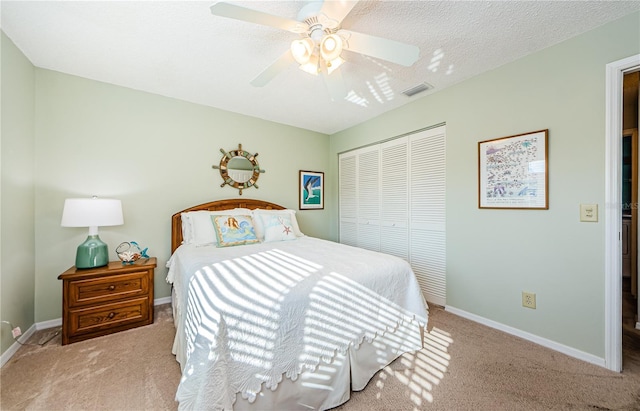 bedroom featuring a textured ceiling, light colored carpet, a closet, and ceiling fan