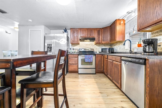 kitchen with appliances with stainless steel finishes, light wood-type flooring, sink, a textured ceiling, and tasteful backsplash