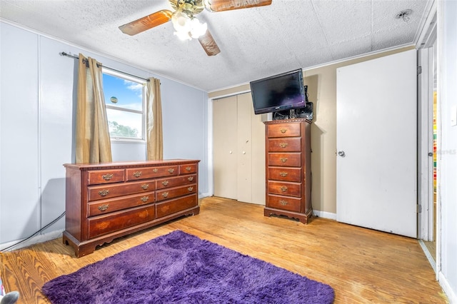 bedroom featuring a closet, light wood-type flooring, ceiling fan, ornamental molding, and a textured ceiling