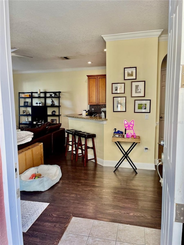 interior space featuring a breakfast bar, wood-type flooring, ornamental molding, kitchen peninsula, and a textured ceiling