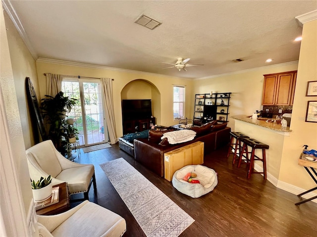 living room with dark hardwood / wood-style flooring, ceiling fan, ornamental molding, and a healthy amount of sunlight