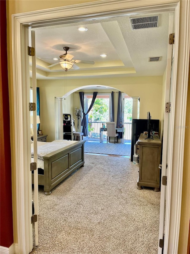 carpeted bedroom with access to exterior, a tray ceiling, and ornate columns