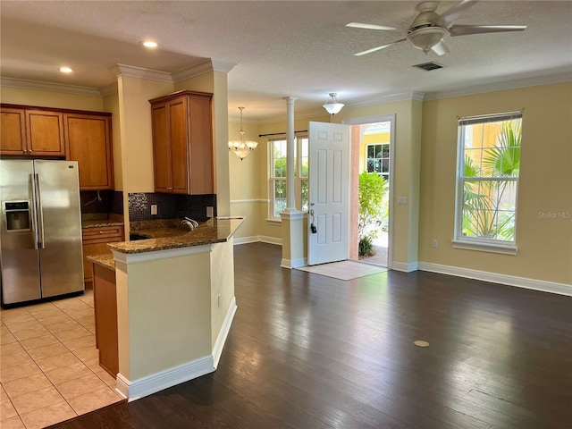 kitchen featuring visible vents, stainless steel refrigerator with ice dispenser, ornamental molding, brown cabinetry, and ceiling fan with notable chandelier