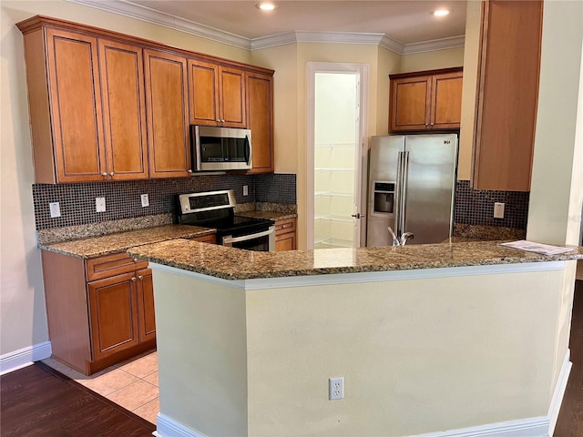 kitchen featuring brown cabinetry, dark stone countertops, appliances with stainless steel finishes, and a peninsula