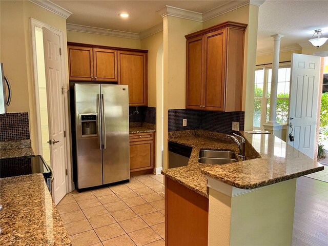 kitchen with a sink, appliances with stainless steel finishes, decorative columns, a peninsula, and brown cabinetry