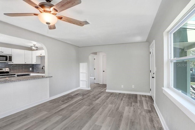 unfurnished living room featuring sink, ceiling fan, light wood-type flooring, and a healthy amount of sunlight