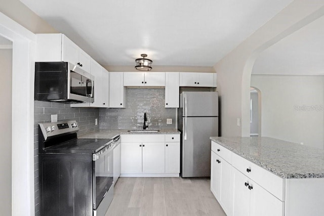 kitchen with light hardwood / wood-style floors, tasteful backsplash, white cabinetry, appliances with stainless steel finishes, and sink