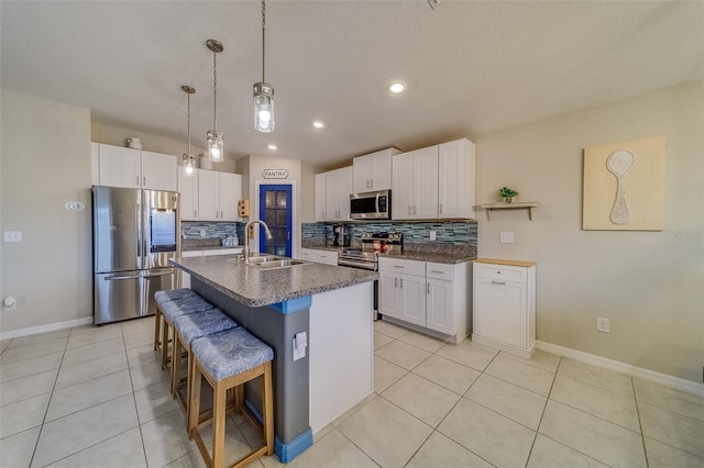 kitchen featuring stainless steel appliances, a breakfast bar, a kitchen island with sink, white cabinets, and sink