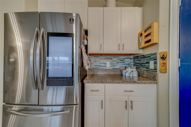 kitchen with dark stone counters, stainless steel fridge, tasteful backsplash, and white cabinetry