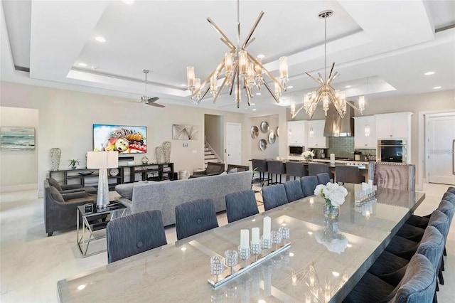 dining area with ceiling fan with notable chandelier and a tray ceiling